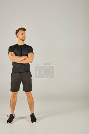 Young athletic man in black t-shirt and shorts working out in studio setting, showcasing strength and fitness.