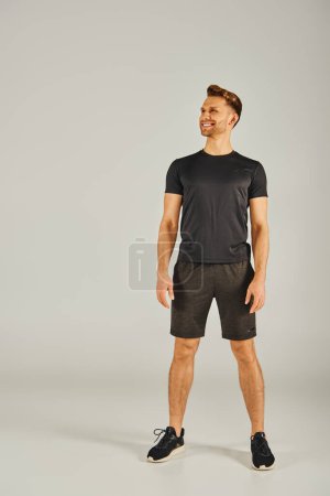 Foto de Un joven atlético vistiendo una camiseta negra y pantalones cortos, haciendo ejercicio en un estudio sobre un fondo gris. - Imagen libre de derechos