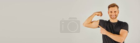 Photo for A young athletic man in active wear showcasing his muscles by flexing his biceps in front of a white background. - Royalty Free Image