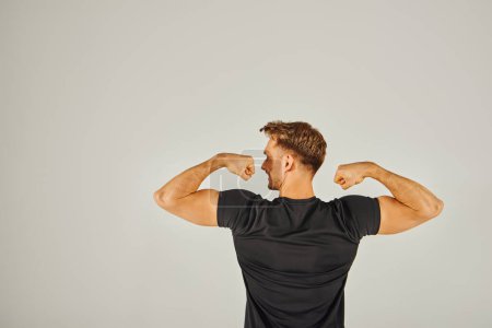 A young athletic man flexes his muscles in front of a white background, showcasing strength and determination.