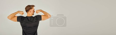 Ein junger, athletischer Mann in aktiver Kleidung lässt vor grauem Hintergrund in einem Studio seine Muskeln spielen.