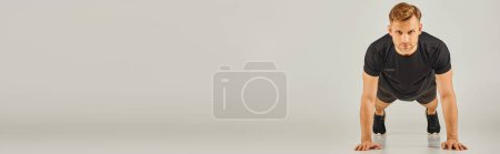 Téléchargez les photos : Un jeune homme athlétique en tenue active effectuant des pompes sur fond gris dans un studio. - en image libre de droit