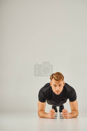 Ein junger, athletischer Mann in aktiver Kleidung, der Liegestütze vor grauem Hintergrund in einem Studio macht.