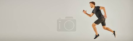 Téléchargez les photos : Un jeune homme athlétique en tenue active courant énergiquement sur fond gris dans un décor de studio. - en image libre de droit