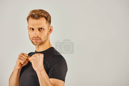 A young athletic man in active wear confidently poses with his fists clenched, exuding strength and determination.