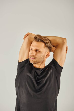 A young athletic man in a black t-shirt strikes a pose against a grey background in a studio setting.
