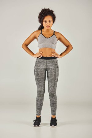 Foto de Ajuste mujer afroamericana en leggings grises con estilo posa con confianza contra un fondo gris en un entorno de estudio. - Imagen libre de derechos