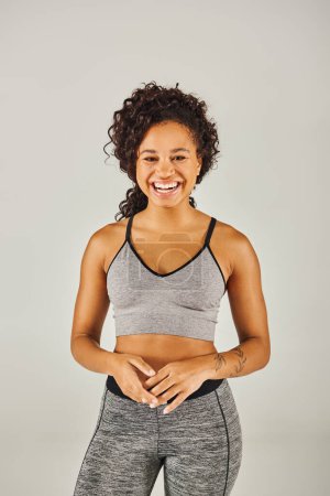 Téléchargez les photos : Jeune femme afro-américaine en tenue athlétique élégante grise et noire travaillant en studio. - en image libre de droit