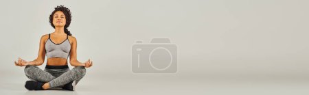 Téléchargez les photos : Une jeune femme afro-américaine en tenue active médite sur un fond gris dans un cadre serein et paisible. - en image libre de droit