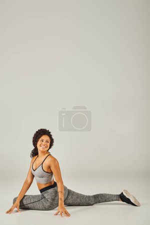 Photo for A young African American woman in active wear gracefully performs a yoga pose on a white background. - Royalty Free Image