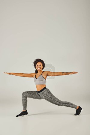 Photo for A young African American woman dressed in activewear gracefully performs a yoga pose on a white background. - Royalty Free Image