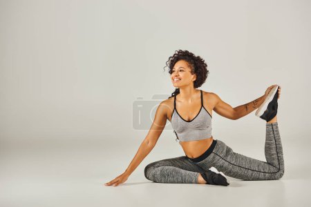 Junge Afroamerikanerin in aktiver Kleidung nimmt anmutig eine Yoga-Pose auf weißem Hintergrund ein.