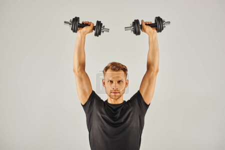 Foto de Un joven deportista en activo lleva pesas de elevación en un estudio sobre un fondo gris. - Imagen libre de derechos