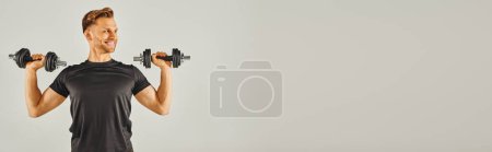 Téléchargez les photos : Un jeune sportif en tenue active tient une paire d'haltères dans un studio avec un fond gris. - en image libre de droit