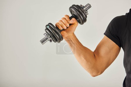 Un joven deportista en activo agarra un par de pesas, centrándose en su entrenamiento en un estudio de fondo gris.