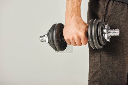 A young sportsman in active wear grips a pair of dumbbells in a studio with a grey background, showcasing strength and determination.