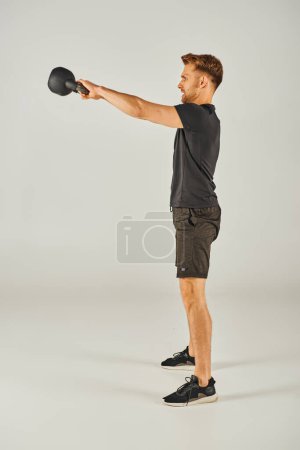 Young sportsman in active wear showcasing strength and determination with kettlebell on white background.
