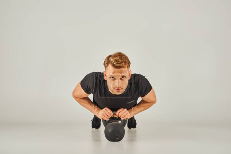 Téléchargez les photos : Un jeune sportif en tenue active soulevant une kettlebell sur fond blanc dans une salle de fitness. - en image libre de droit