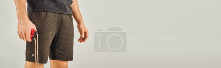 Photo for A young sportsman in active wear holding a skipping rope in a studio with a grey background. - Royalty Free Image