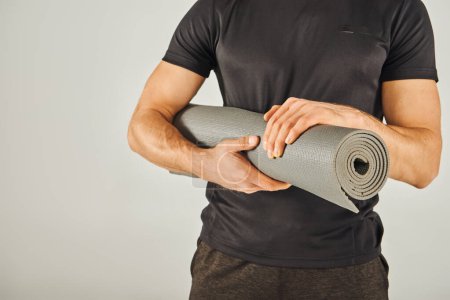 Photo for Young sportsman in active wear holds a yoga mat in a studio with a grey background. - Royalty Free Image