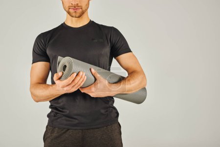 Foto de Joven deportista en ropa activa sosteniendo una esterilla de yoga en un estudio con un fondo gris. - Imagen libre de derechos