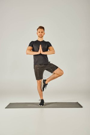 Foto de Joven deportista en ropa activa practicando una pose de yoga sobre un fondo gris. - Imagen libre de derechos