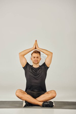 Photo for Young sportsman in active wear gracefully practicing a yoga pose in a studio with a gray background. - Royalty Free Image