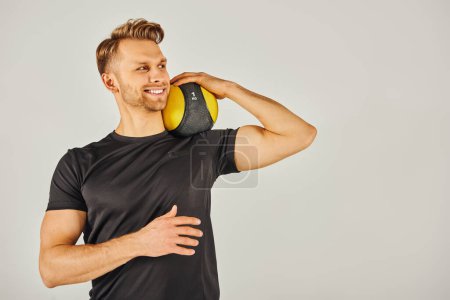 Foto de Un joven deportista en ropa activa sosteniendo una pelota amarilla, mostrando equilibrio y enfoque en un estudio con un fondo gris. - Imagen libre de derechos
