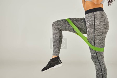 Foto de Una deportista con el pelo rizado lleva leggins de banda verde mientras hace ejercicio en un estudio con un fondo gris. - Imagen libre de derechos