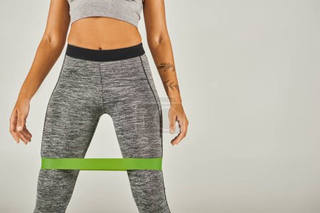 African American sportswoman in green band and leggings, working out in studio with grey background.