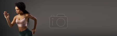Téléchargez les photos : Sportive afro-américaine bouclée en top pratique rose dans un studio sur fond gris. - en image libre de droit