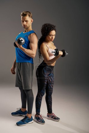 Fit man and woman in active wear posing confidently with dumbbells on a grey studio background.