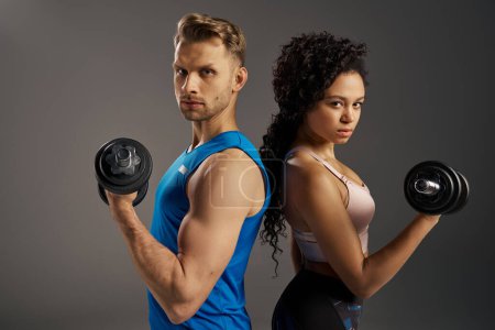 Photo for A fit and multicultural young couple poses confidently with dumbbells in an active wear studio setting. - Royalty Free Image