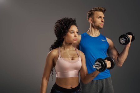 Multicultural man and woman in active wear pose confidently with dumbbells in a studio setting.