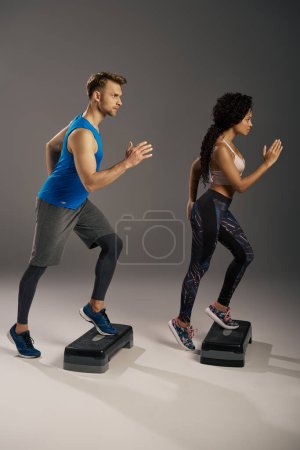 Photo for A young multicultural couple in active wear running energetically on steppers in a studio setting. - Royalty Free Image