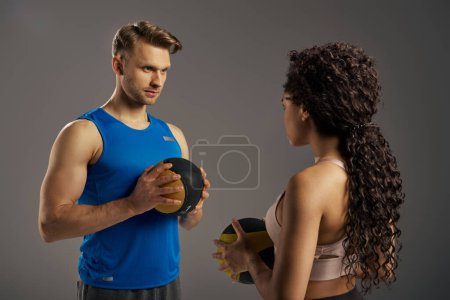 A multicultural couple in active wear grips a weighted ball, showcasing strength and determination in a studio setting.