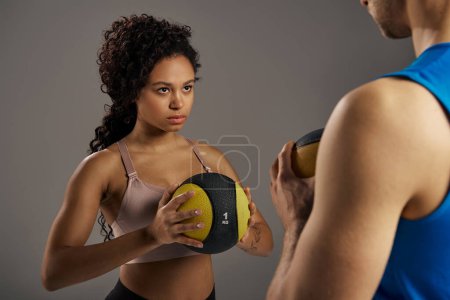 A young multicultural and fit couple in active wear holding yellow balls in a studio setting on a grey background.