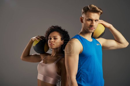 Young multicultural couple in active wear pose with balls in studio setting.