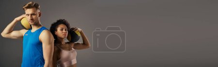 Photo for A young, multicultural couple in active wear posing confidently for the camera against a grey studio backdrop. - Royalty Free Image