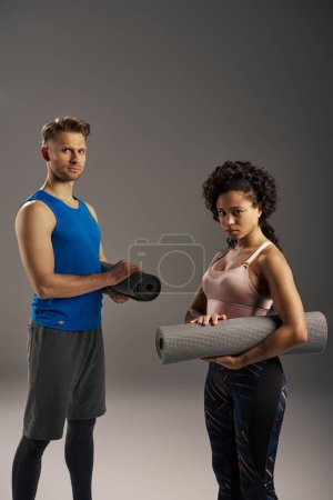Young multicultural couple in active wear standing gracefully next to a yoga mat in a studio setting.