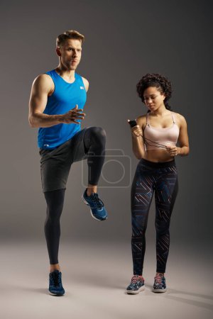A young multicultural and fit couple stand next to each other in active wear, exuding confidence and strength in a studio setting.
