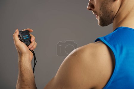 A man in a blue tank top is seen holding an electronic timer.