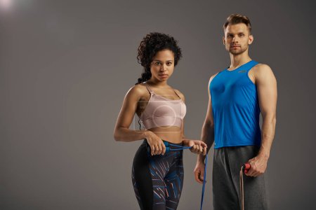 Téléchargez les photos : Un couple multiculturel en tenue de sport pose pour une vidéo de fitness, mettant en valeur leur force et leur vitalité en studio. - en image libre de droit