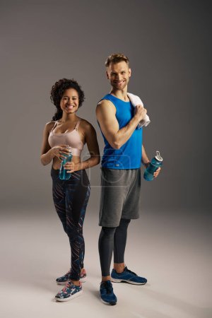 Téléchargez les photos : Un jeune couple multiculturel en tenue active, en pleine forme, posant en toute confiance dans un studio sur fond gris. - en image libre de droit