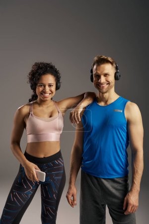 Foto de Una pareja multicultural en forma de ropa deportiva golpea una pose juntos en un estudio sobre un fondo gris. - Imagen libre de derechos