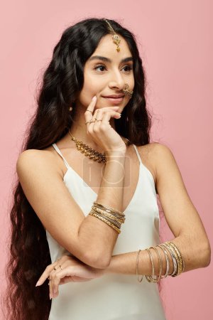 Captivating indian woman with long hair poses with gold jewelry on pink backdrop.