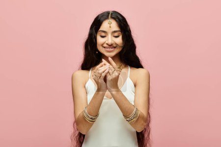 Young indian woman praying in front of vibrant pink backdrop.