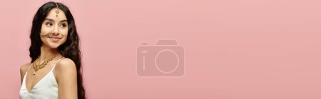 Téléchargez les photos : Une superbe femme indienne dans une robe blanche fluide frappe une pose sur un fond rose vibrant. - en image libre de droit