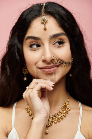 Young indian woman with long hair and gold jewelry striking a pose on a pink background.