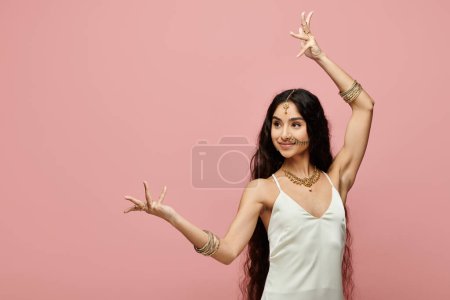 Young indian woman in white dress strikes a pose on vibrant pink background.